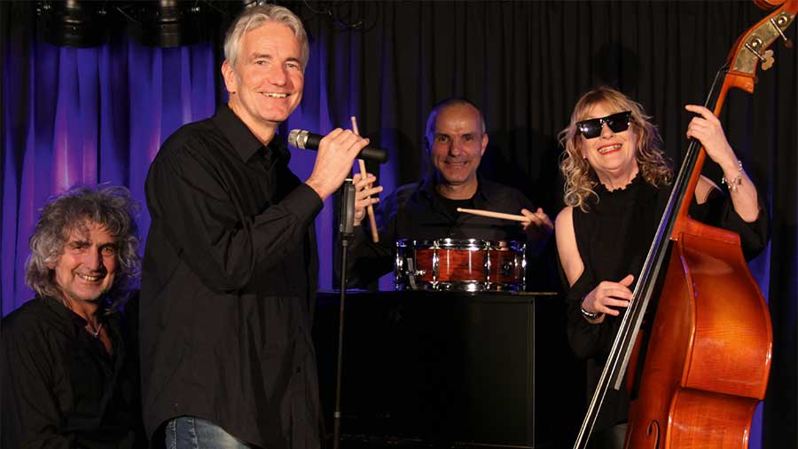 Drei Männer und eine Frau in schwarzer Kleidung mit Musikinstrumenten