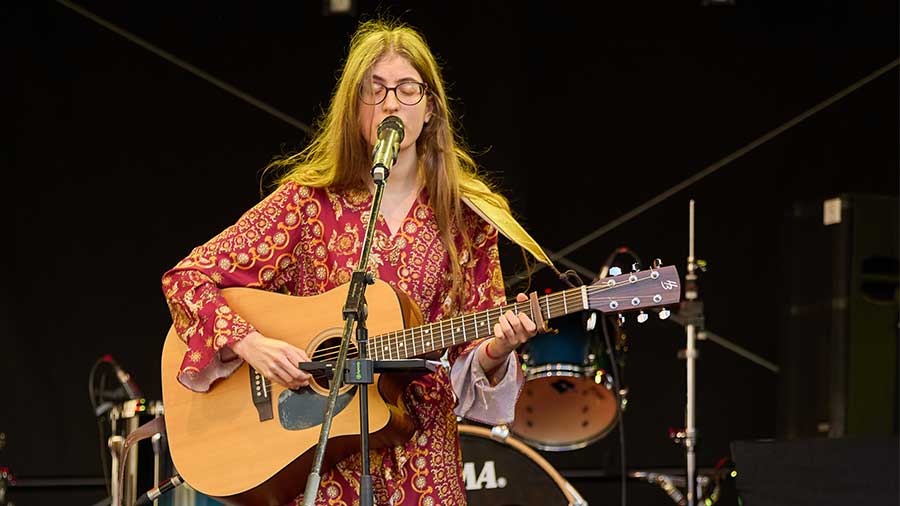 Frau mit Gitarre und Mikrofon alleine auf einer Bühne